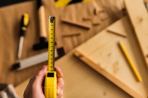 Carpenter with tape measure tool in woodwork workshop interior, close up of hand